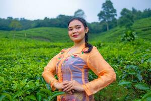 une thé feuille agriculteur dans un Orange robe posant dans de face de une très magnifique thé jardin photo