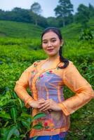 une thé feuille agriculteur dans un Orange robe posant dans de face de une très magnifique thé jardin photo