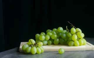 grappes de vert mûr les raisins sur une en bois planche. sur une foncé Contexte. encore la vie haute définition la photographie photo