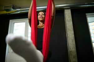 bas vue de une Jeune africain svelte corps femme élongation sa jambes tandis que Faire en volant yoga des exercices photo