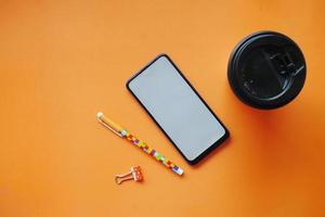 vue de dessus du téléphone intelligent, tasse à thé et stylo sur fond orange