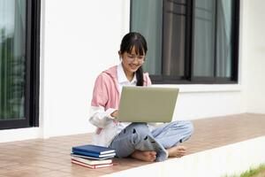 étudiant fille content en train d'étudier en ligne, retour à école concept. Jeune femme étudiant occupé étude faire Remarques dans carnet et en utilisant portable concentré en ligne formation cours La technologie éducation. photo