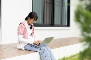 étudiant fille content en train d'étudier en ligne, retour à école concept. Jeune femme étudiant occupé étude faire Remarques dans carnet et en utilisant portable concentré en ligne formation cours La technologie éducation. photo