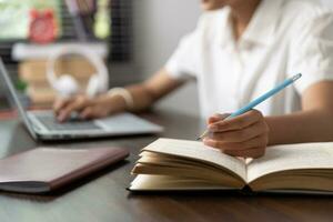 étudiant fille content en train d'étudier en ligne, retour à école concept. Jeune femme étudiant occupé étude faire Remarques dans carnet et en utilisant portable concentré en ligne formation cours La technologie éducation. photo