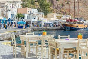 chaises et les tables de une traditionnel grec taverne, restaurant à le Dock de petit Port de flou voile bateau et touristique veille et magasins avec blanc architecture dans Santorin Grèce photo