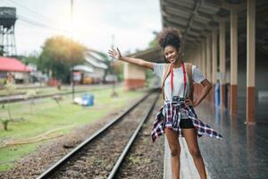 Jeune asiatique africain femme voyageur avec sac à dos dans le chemin de fer train gare, voyageur fille en marchant supporter asseoir attendre prendre une image sur chemin de fer Plate-forme train gare. haute qualité photo