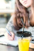 proche en haut de Frais Orange jus dans Plastique tasse avec couvercle et paille, sur étudiants bureau. photo