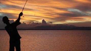 silhouette de une pêcheur avec une pêche barre dans le Lac à le coucher du soleil photo