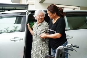 le soignant aide une patiente asiatique âgée handicapée à monter dans sa voiture, concept médical. photo