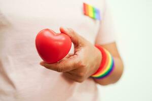 asiatique femme en portant rouge cœur avec arc en ciel drapeau, lgbt symbole droits et le sexe égalité, lgbt fierté mois dans juin. photo