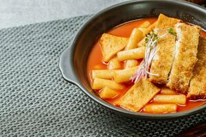 tteokbokki, une épicé coréen plat de porc côtelettes, légumes, et poisson Gâteaux servi sur une noir plaque. photo