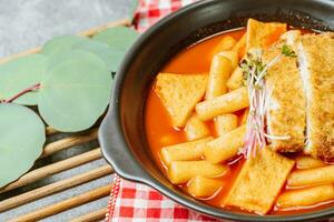 tteokbokki, une épicé coréen plat de porc côtelettes, légumes, et poisson Gâteaux servi sur une noir plaque. photo