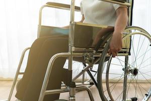 jeune femme handicapée asiatique avec un sentiment heureux et plein d'espoir assis sur le fauteuil roulant seul dans la maison. concept de handicap et d'invalidité photo