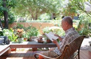 senior asiatique retraité assis sur un banc et lisant un livre à la maison arrière-cour pendant le temps libre