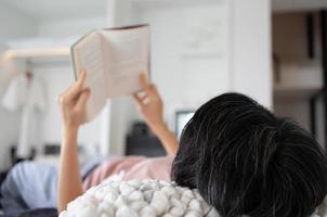 Femme d'âge moyen allongée sur le lit et lisant un livre à l'hôtel pendant les vacances