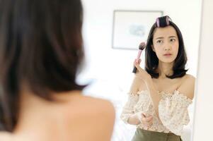 magnifique Jeune asiatique femme appliquant maquillage dans de face de le miroir. mode de vie gens concept. publicité pour peau crème, anti-rides crème, bébé visage photo