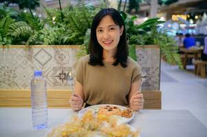 souriant Jeune asiatique femme profiter repas tel comme américain frit riz et frit palourdes dans une restaurant. photo
