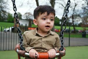 mignonne asiatique pakistanais bébé est profiter le magnifique ensoleillé journée à mise en garde les enfants et Publique parc de luton ville de Angleterre Royaume-Uni. faible angle image a été capturé sur avril 03ème, 2023 photo