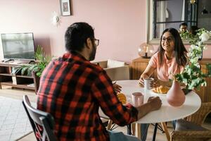 content couple en mangeant petit déjeuner et parlant à à manger table dans Matin. Indien fille et latino gars. relation et la diversité concept photo