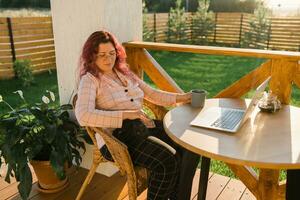 femme travail avec portable Extérieur dans été terrasse avec noir chaton. fille et chat en train de regarder vidéo sur ordinateur dans le soir. travail de maison, entreprise, animal de compagnie et mode de vie concept. photo