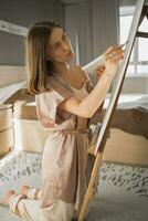 Jeune femme artiste La peinture sur Toile sur le chevalet à Accueil dans chambre - art et la créativité concept photo