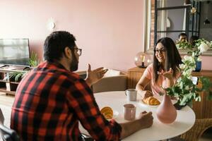 Jeune diverse aimant couple en mangeant croissant et pourparlers ensemble à Accueil dans petit déjeuner temps. la communication et relation concept photo
