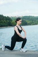 Jeune femme dans noir tenue de sport exercice en plein air. aptitude et en bonne santé mode de vie concept. le blanc fille Est-ce que des sports dans le parc. photo