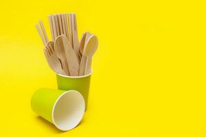 jetable en bois cuillères, fourches et des couteaux dans une vert papier tasse sur une Jaune Contexte avec espace de copie, recyclé. photo