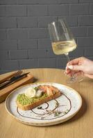 verre de blanc du vin dans femelle main et pain grillé avec saumon, Avocat et poché Oeuf photo