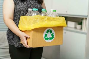 Accueil recycler éco vert zéro concept femme lancement vide Plastique bouteille dans recyclage poubelle avec Jaune des ordures Sacs à maison. photo