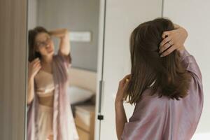 content Matin. attrayant Jeune femme à la recherche dans miroir à sa appartement photo