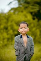 mignonne peu garçon une bien habillé garçon dans une costume dans une arrière-cour avec une pelouse et à la recherche pour quelque chose intéressant. photo