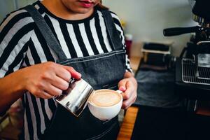 fermer de le main de une professionnel barista dans une café magasin fabrication verser à la vapeur Lait dans le café tasse fabrication cappuccino menu photo