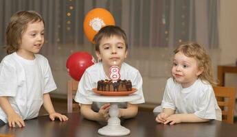 Trois les enfants séance à une table avec une gâteau photo