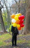 une homme permanent dans une parc en portant une bouquet de des ballons photo