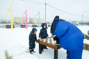 une homme et deux les enfants en jouant échecs dans le neige photo