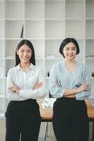 portrait de Jeune souriant deux femme à la recherche à caméra avec franchi bras. content deux fille permanent dans Créatif bureau. réussi femme d'affaires permanent dans Bureau avec copie espace. photo