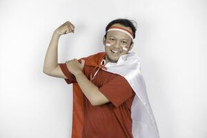 excité asiatique homme portant une rouge haut, drapeau cap et Bandeau, montrant fort geste par levage le sien bras et muscles souriant fièrement. l'indonésie indépendance journée concept. photo