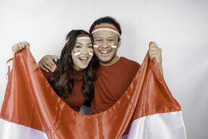 une Jeune asiatique couple avec une content réussi expression portant rouge Haut et Bandeau tandis que en portant l'indonésie drapeau, isolé par blanc Contexte. l'indonésie indépendance journée concept. photo