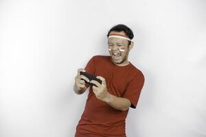 une portrait de une souriant asiatique homme portant Bandeau et en portant le sien téléphone, isolé par blanc Contexte. l'indonésie indépendance journée concept photo