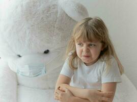 une peu fille séance sur une lit avec une masque sur nounours ours photo