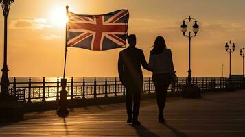 couple en marchant en dessous de Britanique drapeau sur côtier promenade dans Angleterre à le coucher du soleil. silhouette concept photo