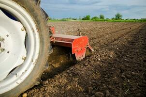 une tracteur avec une coupeur unité est cultiver le champ. ample écrasé humide sol après cultiver avec une cultivateur. relâchement surface, terre cultivation. agriculture. utilisation agricole machinerie photo