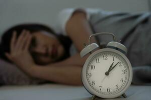 asiatique femme dans lit en retard en essayant à sommeil Souffrance insomnie, sans sommeil ou effrayé dans une cauchemar, à la recherche triste inquiet et stressé. fatigué et mal de crâne ou migraine veille en haut dans le milieu de le nuit. photo