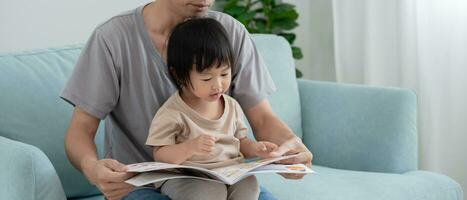 asiatique père se détendre et lis livre avec bébé temps ensemble à maison. parent asseoir sur canapé avec fille et en train de lire une histoire. apprendre développement, garde d'enfants, en riant, éducation, narration, entraine toi. photo