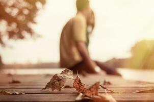 une Jeune couple dans l'amour séance sur une jetée dans une parc avec un l'automne feuille dans le premier plan. photo