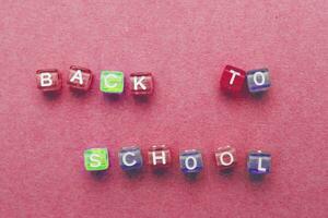 le une inscription retour à école fabriqué par multicolore Plastique cubes sur une rouge rose Contexte. photo