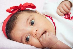 fermer de une sucré un mois bébé fille avec une surprise expression portant une rouge et blanc t chemise. photo