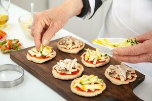 ajouter garnitures à le mini pizzas. ajouter des légumes. délicieux fait maison mini pizzas préparation. photo