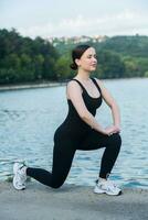 Jeune femme dans noir tenue de sport exercice en plein air. aptitude et en bonne santé mode de vie concept. le blanc fille Est-ce que des sports dans le parc. photo